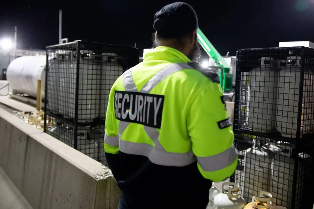 Security officer wearing a high-visibility jacket standing near industrial tanks during a perimeter check in Commerce.