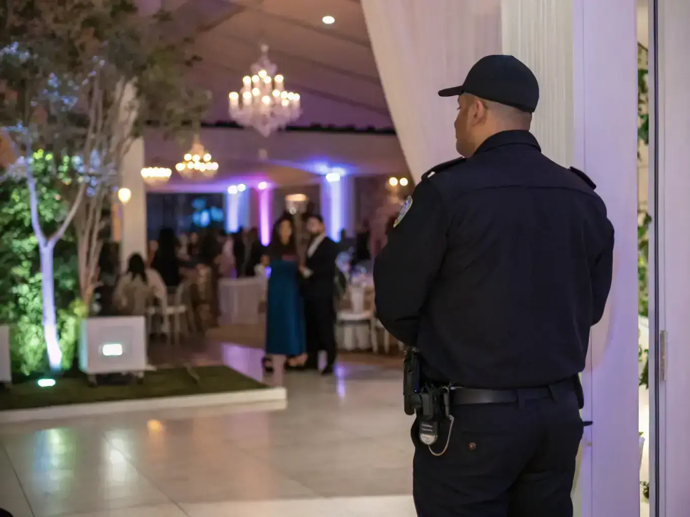 A medium shot of a security guard standing watch at a corporate event in Long Beach, with attendees mingling in the background and the Long Beach skyline visible in the distance, emphasizing the professionalism and reliability of the service.